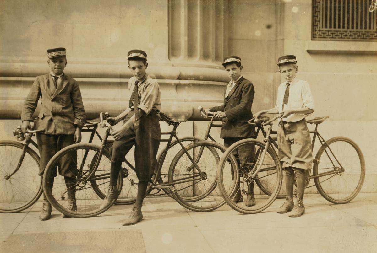 Students in 1940s attire arriving at a school building, some by foot and others by bicycle